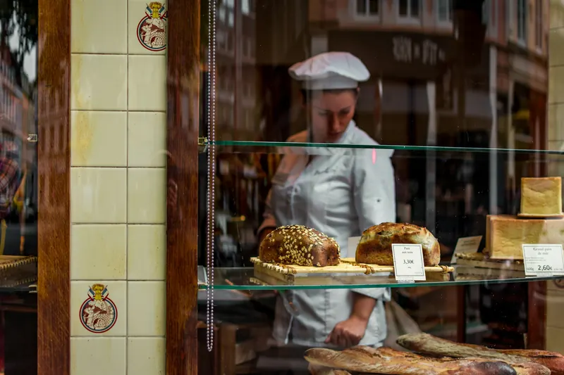 Baker arranging fresh loaves behind a glass bakery display