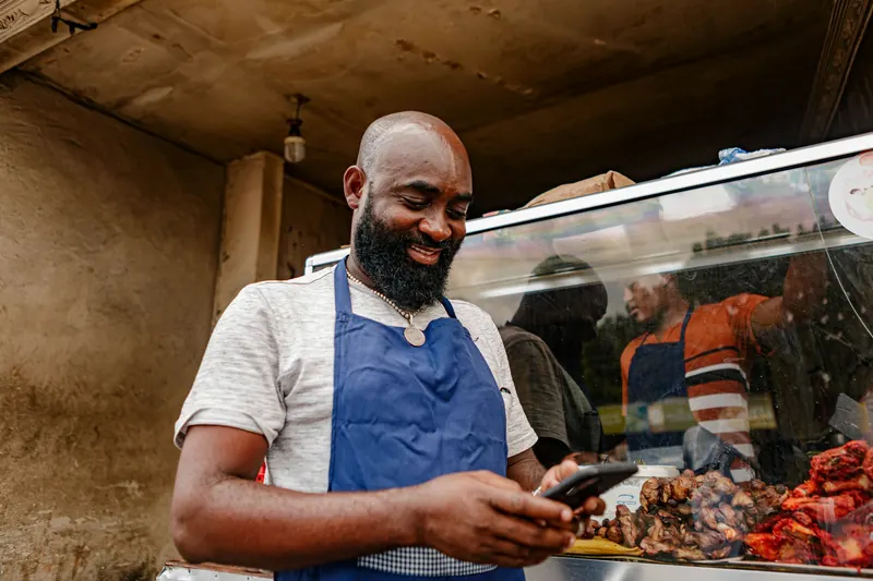 Shop owner in a blue apron checking his phone beside a display case