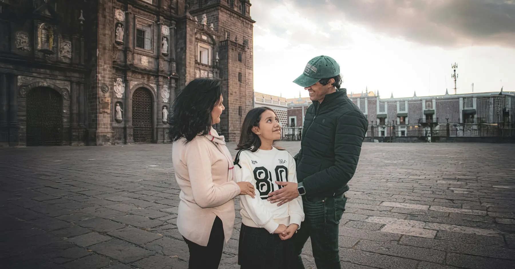 Una madre, un padre y su hija compartiendo un momento feliz en una plaza histórica de piedra