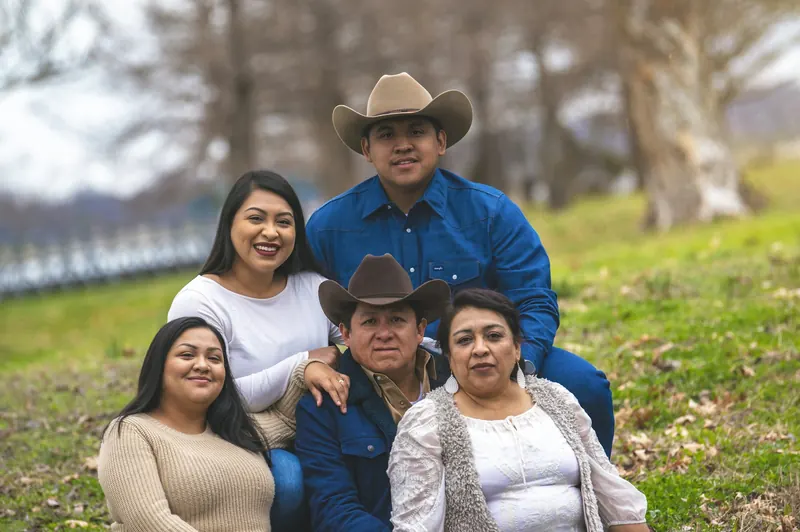 Smiling family of five, parents and grown children, gathered together on a grassy hillside