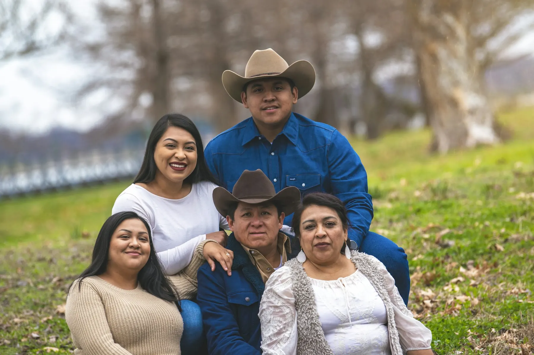Smiling family of five, parents and grown children, gathered together on a grassy hillside