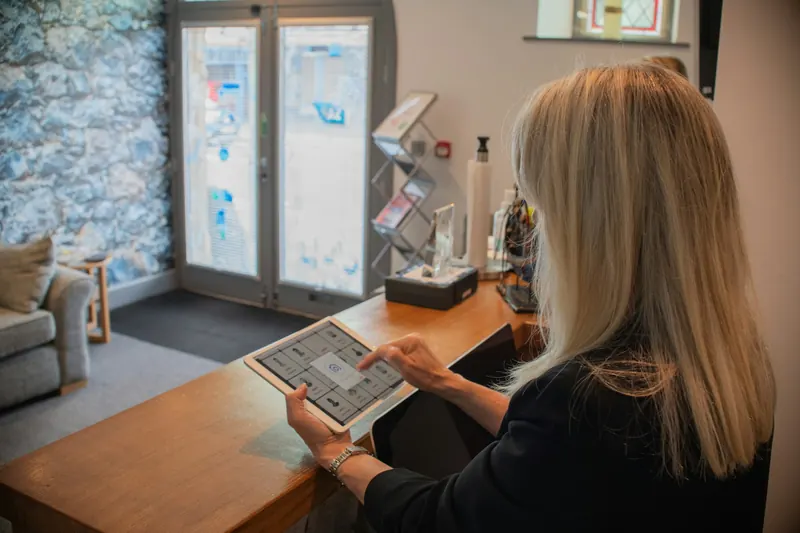 Woman using a tablet check-in screen at a wooden reception desk in a bright office lobby