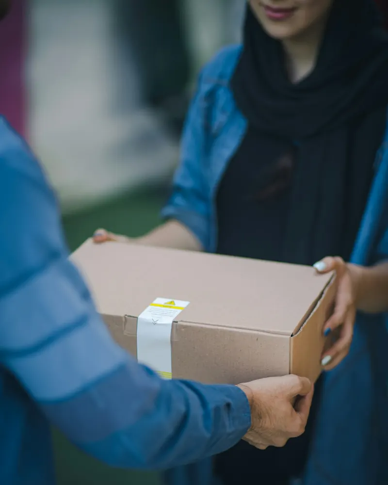 Close-up of a person handing a cardboard parcel to a woman who receives it with both hands