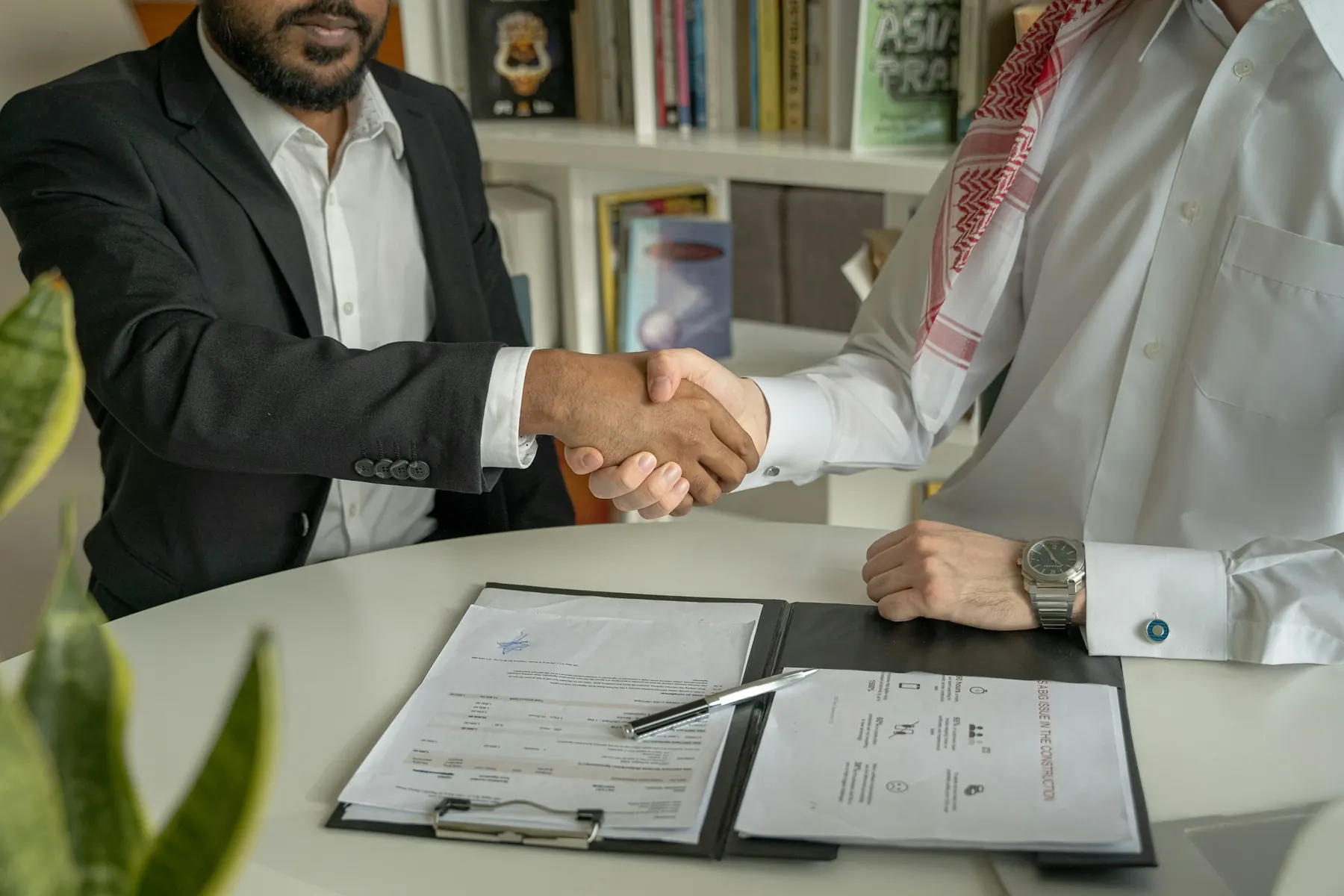 Two business partners shaking hands over a signed agreement
